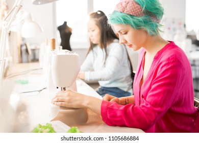 Side view portrait of creative young woman making clothes sitting at sewing machine and working in modern atelier, copy space