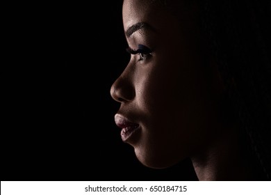 Side view portrait of dark skinned model on a black backstage. Light and shadow portrait of a woman in side view.