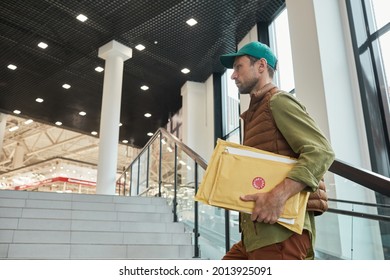 Side view portrait of delivery man holding parcels while walking up stairs to office building, copy space