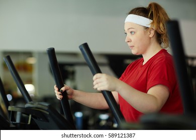 Side View Portrait Of Determined Overweight Woman Working Out In Gym: Using Ellipse Machine With Effort To Lose Weight