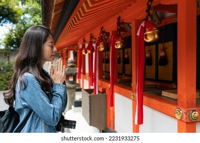 side view portrait of devout asian Japanese girl saying prayers with palms together and eyes close in front of hanging bells at Fushimi Inari Taisha shrine in Kyoto japan - Shutterstock ID 2231933275