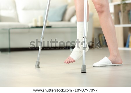 Side view portrait of a disabled woman with bandaged foot walking with crutches at home Imagine de stoc © 