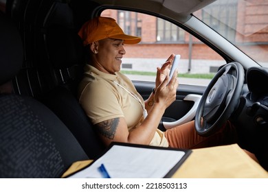 Side View Portrait Of Female Delivery Driver Using Smartphone App In Van