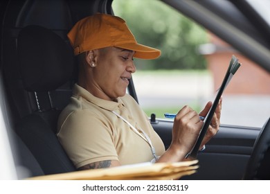 Side View Portrait Of Female Delivery Driver Filling Postal Forms In Van