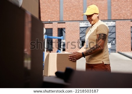 Side view portrait of female delivery worker holding boxes while unloading van trunk, copy space