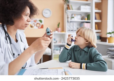 Side view portrait of female pediatrician teaching little boy using inhaler at doctors office - Powered by Shutterstock