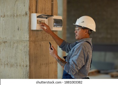Side view portrait of female worker setting up electricity and using smartphone while working on construction site, copy space