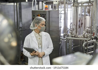 Side View Portrait Of Female Worker Wearing Mask And Holding Digital Tablet During Quality Control Inspection At Food Factory, Copy Space