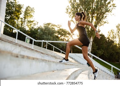 Side View Portrait Of A Fitness Woman In Earphones Running Up The Stairs Outdoors