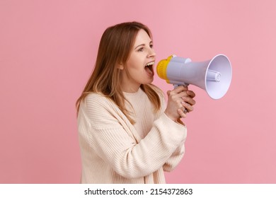 Side View Portrait Of Good Looking Young Blond Woman Yelling In Loud Speaker, Announcing Important Information, Wearing White Sweater. Indoor Studio Shot Isolated On Pink Background.