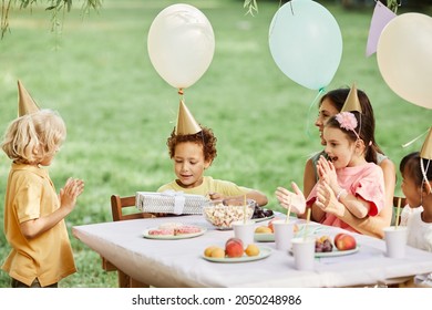 Side View Portrait Of Group Of Kids Enjoying Outdoor Birthday Party In Summer And Giving Gifts