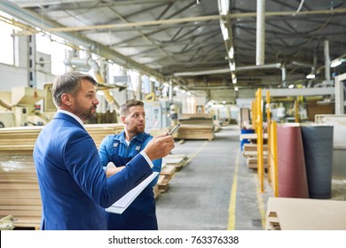 Side view portrait of handsome mature businessman touring modern factory inspecting quality of production, assisted with young workman, copy space