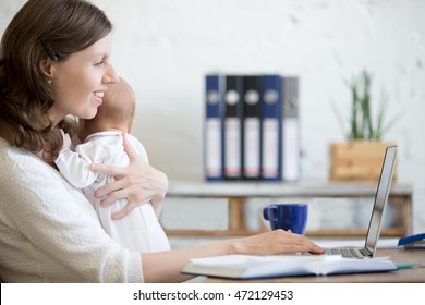 Side View Portrait Of Happy Casual Young Business Mom Holding Her Newborn Cute Babe While Working On Laptop In Home Office Interior. Smiling Working Mother Using Pc Computer And Nursing New Born Child