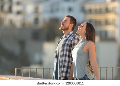 Side view portrait of a happy couple breathing fresh air in a town street