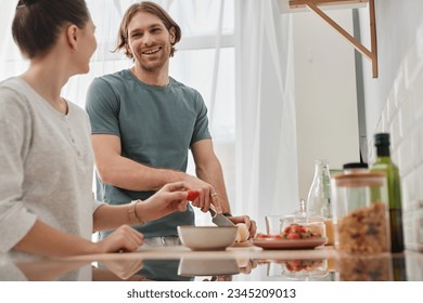 Side view portrait of happy couple making breakfast together in morning focus on young man smiling at girlfriend, copy space - Powered by Shutterstock