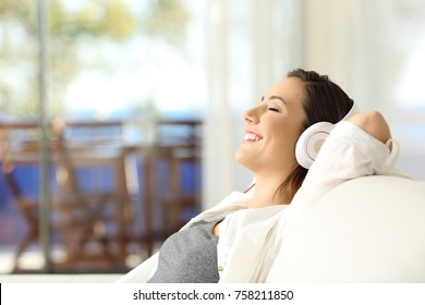 Side view portrait of a happy girl relaxing listening to music sitting on a sofa in the living room in a house interior
