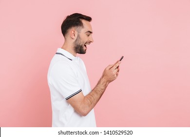 Side View Of Portrait Of A Happy Handsome Man Standing Isolated Over Pink Background, Holding Mobile Phone