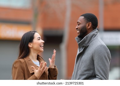Side view portrait of a happy interracial relation with woman and man talking in the street