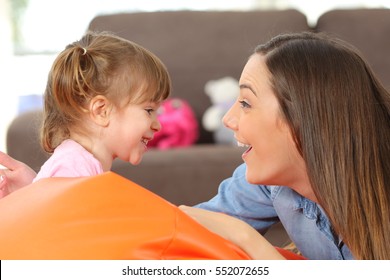 Side view portrait of a happy mother and 2 years baby daughter facing and joking in the living room at home