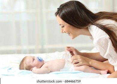Side view portrait of a happy mother changing diaper to her baby