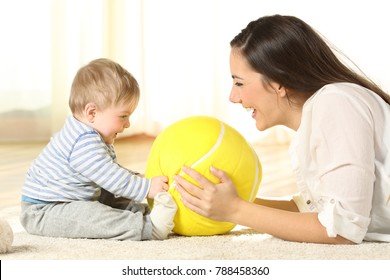 Side View Portrait Of A Happy Mother Playing With Her Baby With A Ball Lying On The Floor At Home