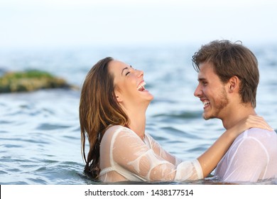 Side View Portrait Of A Happy Spontaneous Couple Joking In The Water On The Beach