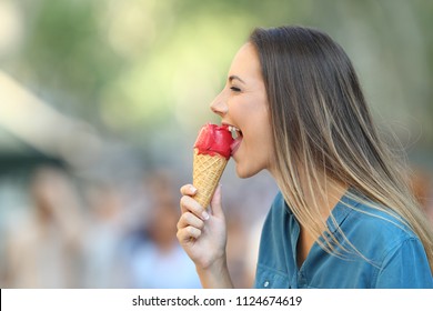 Side view portrait of a happy woman biting an ice cream on the street