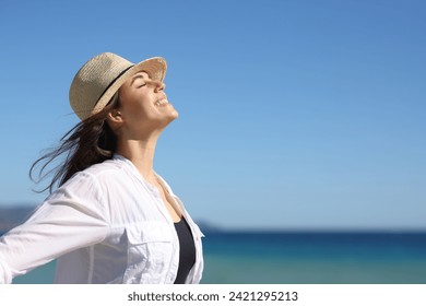 Side view portrait of a happy woman on the beach breathing fresh air wearing hat a summer sunny day - Powered by Shutterstock