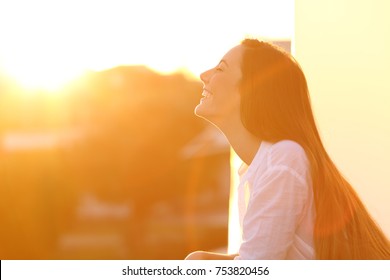 Side view portrait of a happy woman breathing deep fresh air at sunset in a house balcony