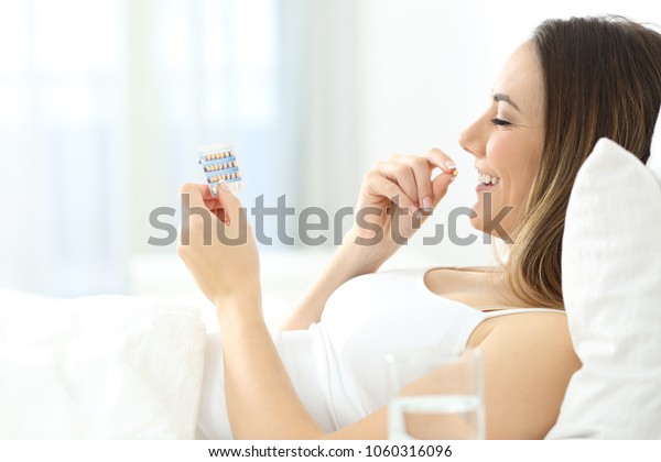 Side view portrait of a happy woman taking contraceptive pill in the bed at home