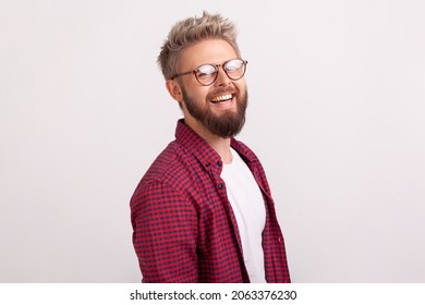 Side View Portrait Of Joyful Bearded Blond Guy In Eyeglasses And Casual Clothes Sincerely Smiling Looking At Camera, Good Mood. Indoor Studio Shot Isolated On Gray Background