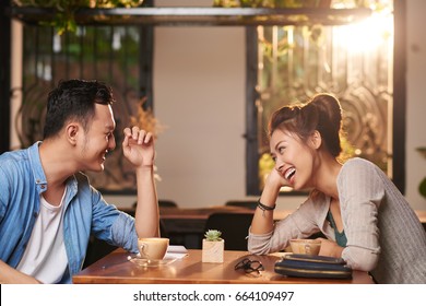 Side view portrait of laughing Asian couple enjoying date in cafe
