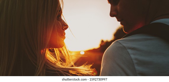 Side view portrait of a lovely couple looking to each other smiling against sunset.