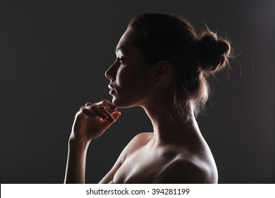 Side view portrait of a lovely woman with fresh skin standing on dark background