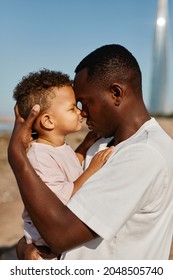 Side View Portrait Of Loving African-American Father Holding Baby Son While Enjoying Walk On Beach