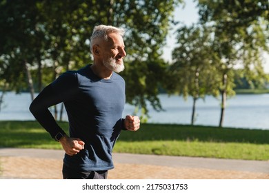 Side view portrait of a male mature athlete sportsman runner jogging in the morning in public park. Slimming exercises, active seniors concept.