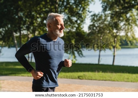 Side view portrait of a male mature athlete sportsman runner jogging in the morning in public park. Slimming exercises, active seniors concept.