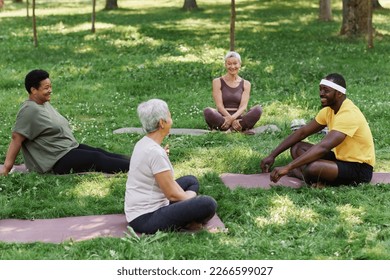 Side view portrait of male yoga instructor coaching outdoor meditation session to group of senior women in park - Powered by Shutterstock