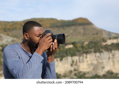 Side view portrait of a man with black skin taking photos with dslr camera in the mountain