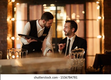 Side view portrait of mature bearded businessman talking to waiter bringing coffee and smiling happily in luxury restaurant, copy space