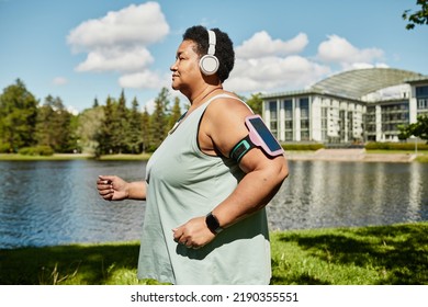 Side View Portrait Of Mature Black Woman Running Outdoors And Wearing Headphones Enjoying Workout