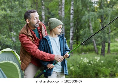 Side View Portrait Of Mature Father Teaching Son Fishing While Enjoying Camping Trip Together By Lake, Copy Space