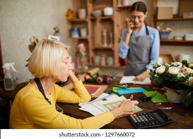 Side View Portrait Of Mature Female Businesswoman Counting Finances Using Calculator In Small Shop, Copy Space