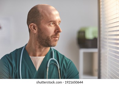 Side View Portrait Of Mature Male Veterinarian Looking At Window Through Blinds At Vet Clinic, Copy Space