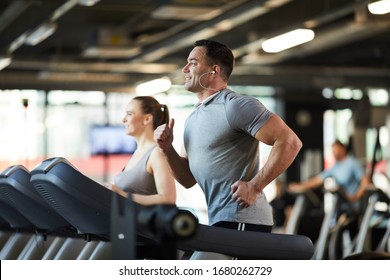 Side View Portrait Of Mature Muscular Man Running On Treadmill While Enjoying Cardio Workout With Music In Modern Gym, Copy Space