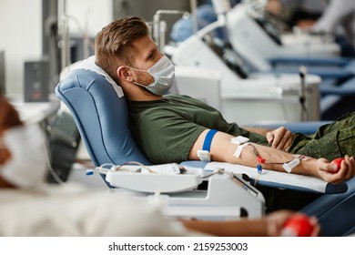 Side View Portrait Of Military Soldier Donating Blood While Lying In Chair At Donation Center And Wearing Mask, Copy Space