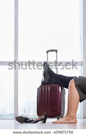 Side view portrait  of modern Asian  business people, man and woman, waiting for departure on business trip  in airport with big suitcases, sitting against flight information display