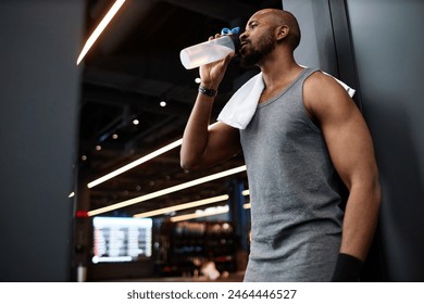 Side view portrait of muscular Black man drinking water after training in gym interior, copy space - Powered by Shutterstock