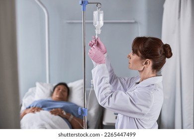 Side view portrait of nurse adjusting IV fluid setup in hospital while caring for patients - Powered by Shutterstock