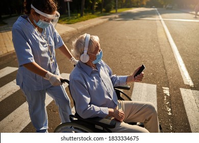 Side View Portrait Of Older Man In Headphones Listening Something While Woman Medical Worker Walking With Him In The City